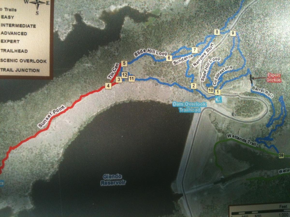 A detailed map showing various hiking and biking trails around Glendo Reservoir, with color-coded paths indicating difficulty levels: red for easy (Sunset Point), blue for intermediate to expert trails, and green for the Wetlands Trail. Key features include trail junctions, scenic overlooks, and trailheads like the Dam Overlook Trailhead. Glendo State Park mountain bike trail.