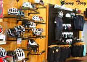A display of various bicycle helmets and cycling apparel on wooden shelves in a shop, featuring different styles and sizes of helmets, along with shirts and shorts designed for biking.