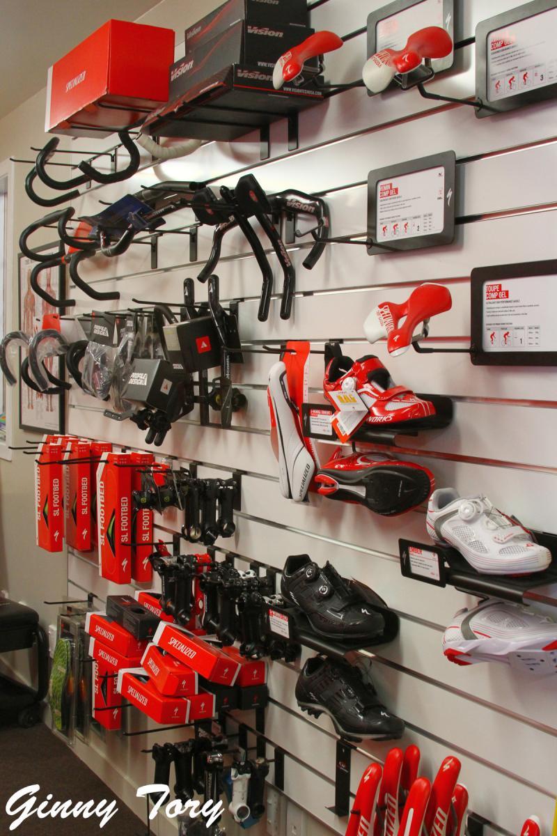 A display wall featuring various cycling accessories, including handlebars, bike seats, and cycling shoes. The items are neatly organized on racks, with brand labels visible. The color scheme includes red, black, and white, showcasing gear from a well-known cycling brand.