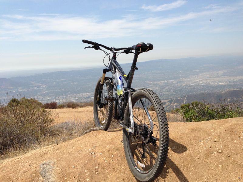 A mountain bike parked on a dirt trail with a scenic view of a valley and distant hills under a clear blue sky. La Tuna Canyon mountain bike trail.