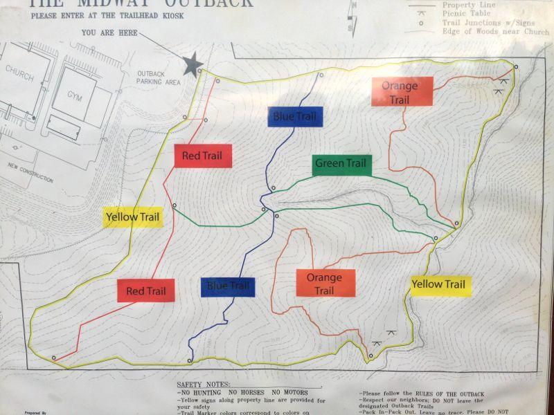 A trail map of The Midway Outback, featuring various colored hiking trails, including Red, Blue, Green, Orange, and Yellow. Key landmarks like the church and gym are noted, along with an "Outback Parking Area." Safety notes regarding trail use and access are included at the bottom. The location of the trailhead kiosk is marked with a star, indicating the starting point for visitors. Midway Outback mountain bike trail.