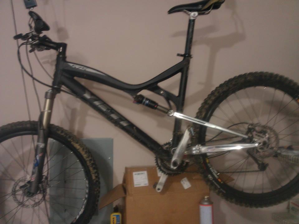 Yeti 575: Mountain bike hanging on a wall in a garage, featuring a black frame, silver components, and thick, knobby tires. A cardboard box and other items are visible in the background.