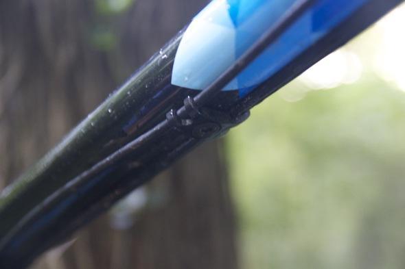 Ragley Blue Pig: Close-up image of a black archery bow with blue details, showcasing the grip and string attachment under soft, natural lighting. The background is blurred, suggesting an outdoor setting with greenery.