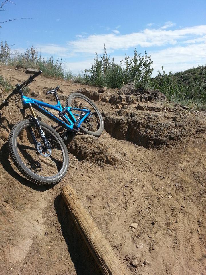 A blue mountain bike resting on rocky, sandy terrain with sparse vegetation and a clear blue sky in the background. White Ranch mountain bike trail.