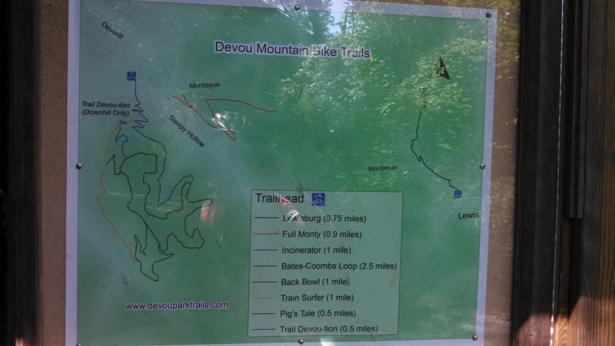 Map of Devou Mountain Bike Trails showing various bike trails including Lewisburg, Full Monty, Incinerator, Bates-Coombs Loop, Back Bowl, Train Surfer, Pig's Tale, and Trail Devou-tion. The map features trail lengths and directional markers, with a green background and overlaid trails illustrated in different colors. Devou Park mountain bike trail.