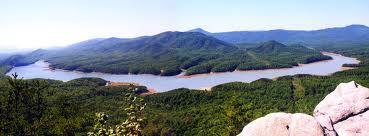 A panoramic view of a river meandering through lush green hills and mountains under a clear blue sky. The scene captures the natural beauty of the landscape, highlighting the harmony between water and vegetation. Carvin's Cove Trail system mountain bike trail.