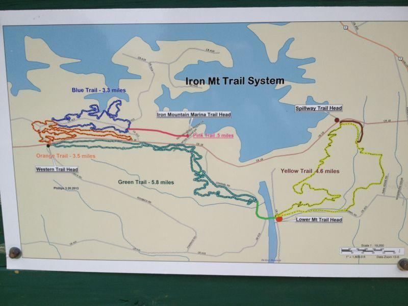 Map of the Iron Mountain Trail System, featuring various trails marked in different colors, including the Blue Trail (3.3 miles), Orange Trail (3.5 miles), Green Trail (5.8 miles), Yellow Trail (4.6 miles), and Pink Trail (5 miles). It also shows key locations such as the Iron Mountain Marina Trail Head and Spillway Trail Head. Iron Mountain mountain bike trail.