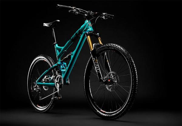 Yeti SB66c: A turquoise mountain bike with a sleek frame and sturdy tires, positioned against a dark background. The bike features prominent suspension components, disc brakes, and a detailed gear system, showcasing its design for rugged terrain.