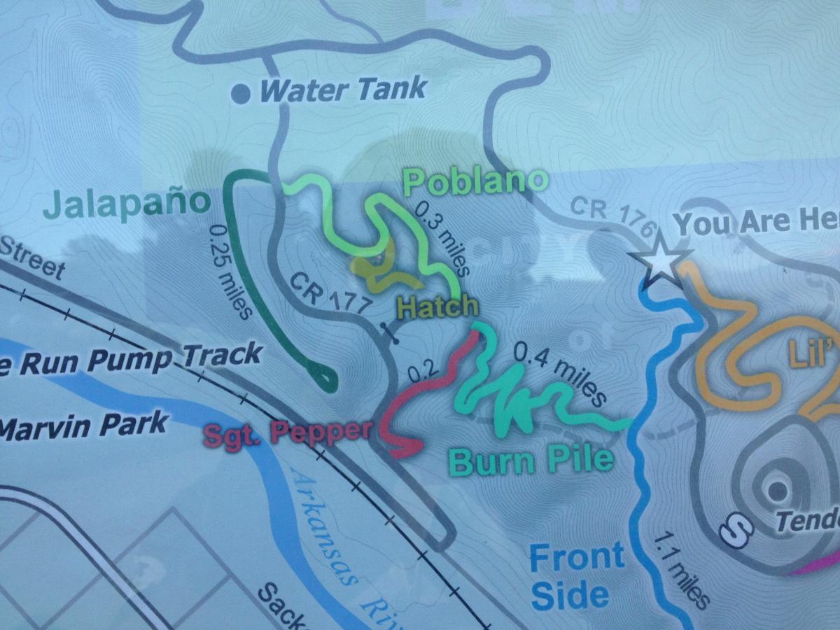 Map displaying hiking trails and distances at a recreational area, with trails labeled Jalapeño, Poblano, Hatch, Burn Pile, and Sgt. Pepper. Other features include a water tank, a pump track, and notable landmarks such as "You Are Here." Arkansas Hills mountain bike trail.