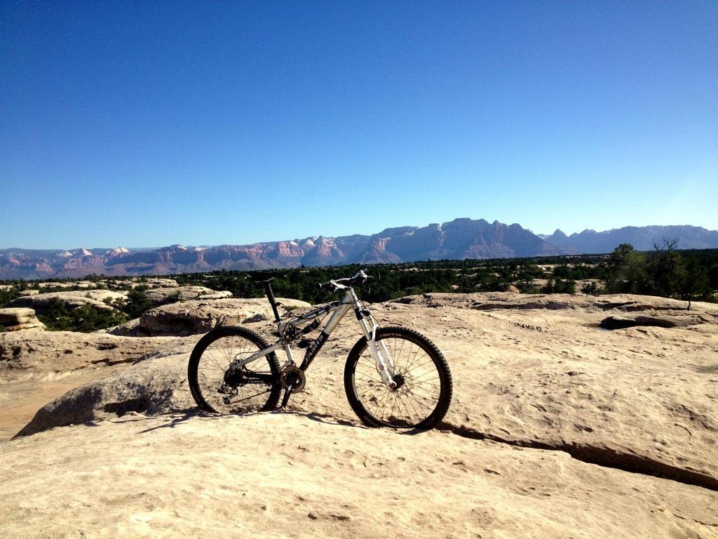 A mountain bike resting on rocky terrain with a scenic view of mountains and blue sky in the background. Gooseberry Mesa mountain bike trail.