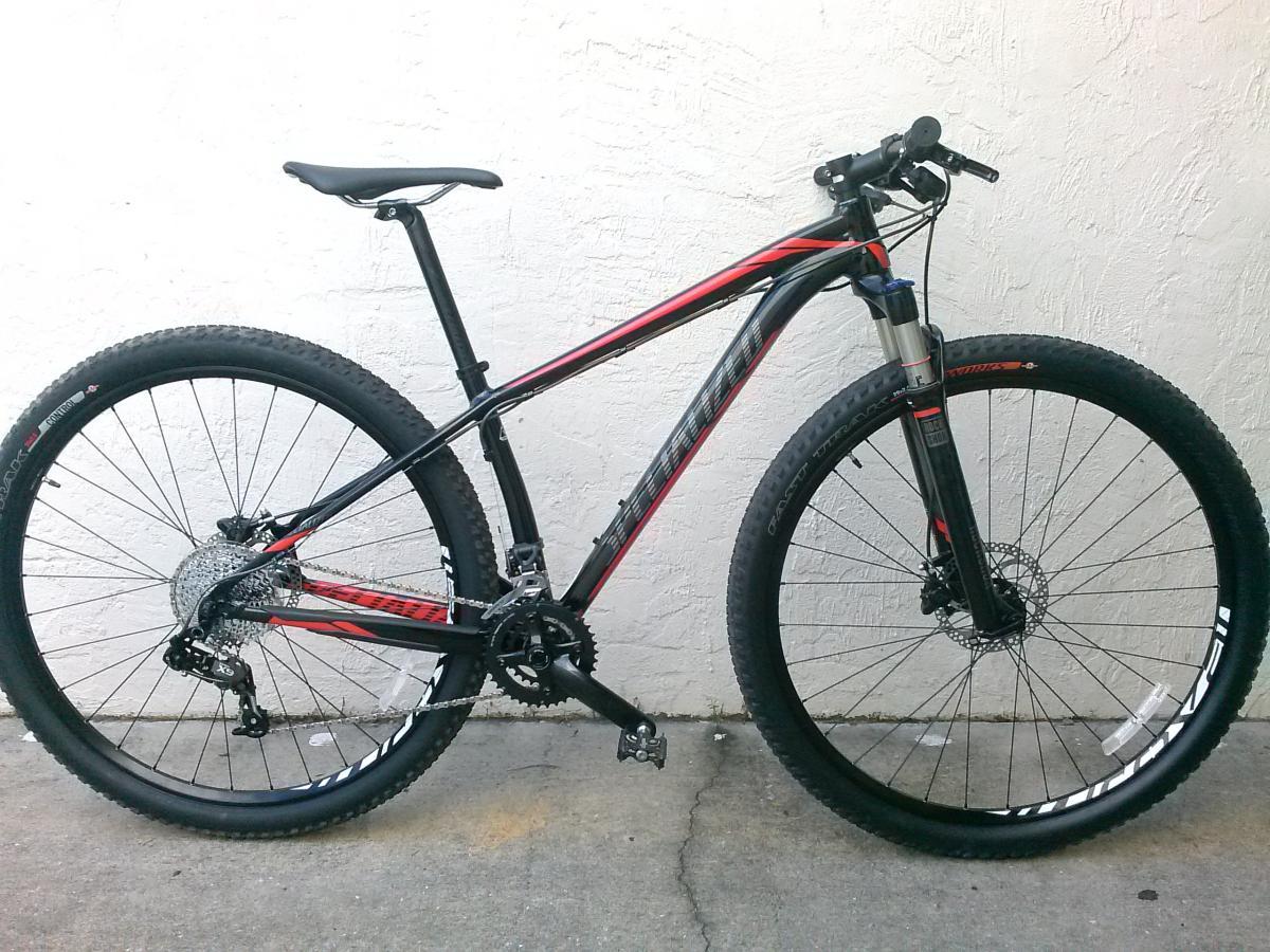 Specialized Stumpjumper Comp 29er: A mountain bike with a black and red frame, featuring thick tires and a front suspension, positioned against a light-colored wall.