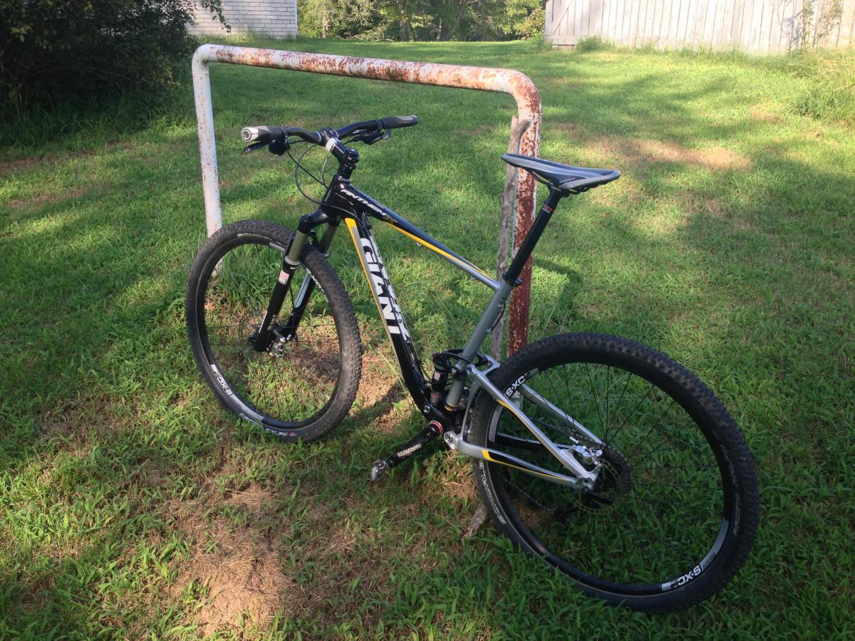 Giant Anthem X 29er 2: A mountain bike leaning against a rusted soccer goalpost, set in a grassy field with trees in the background.