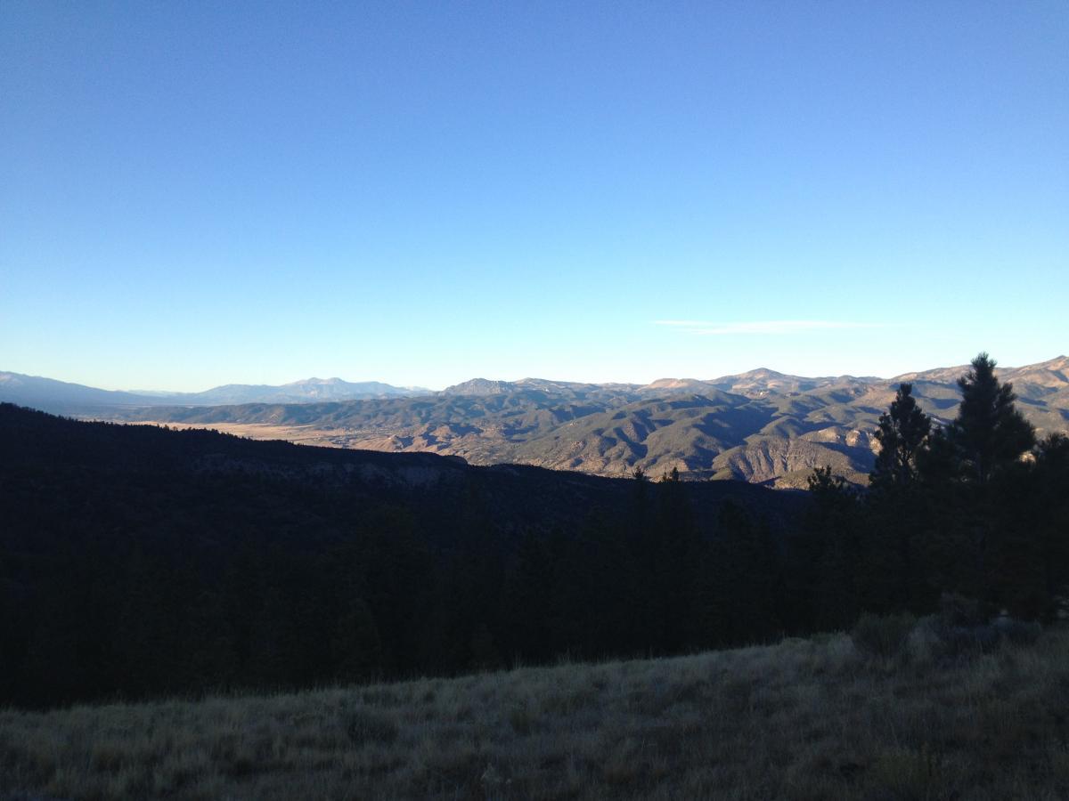 A scenic view of rolling mountains under a clear blue sky, with foreground grass and trees. The landscape features a valley and varying elevations, showcasing the natural beauty of the area. Rainbow Trail: Methodist Mountain Thd to Bear Creek Thd mountain bike trail.