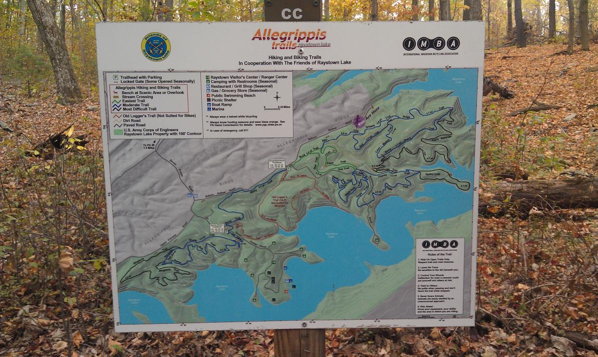 A map of the Allegrippis Trails at Raystown Lake, displaying various hiking and biking trails, parking locations, and points of interest. The map includes different trail difficulties, trailheads, and nearby facilities such as a visitor center, picnic areas, and a boat ramp, all set against a background of autumn foliage. Allegrippis Trails mountain bike trail.