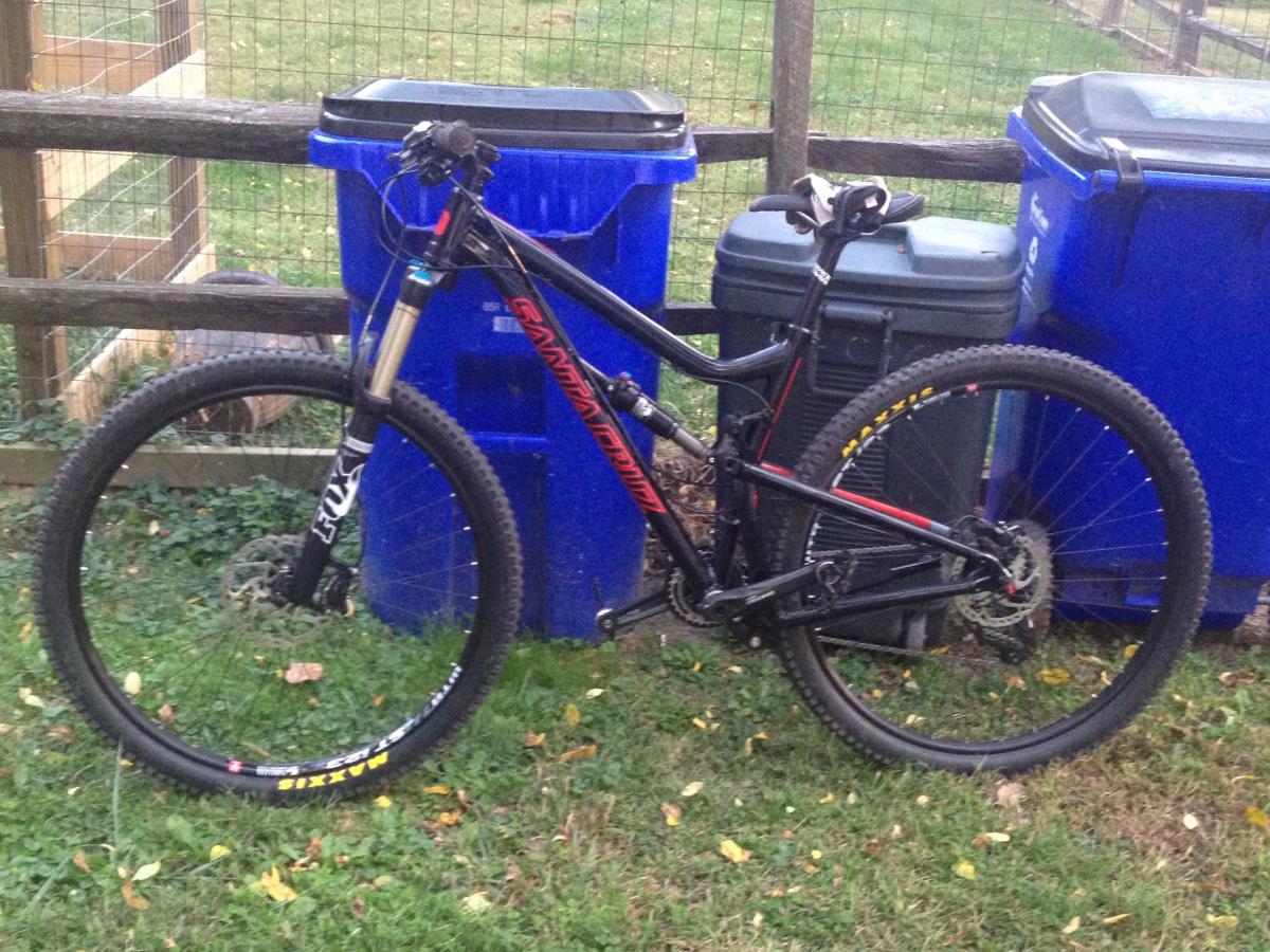 Santa Cruz Tallboy LT: A black mountain bike with red accents leaning against two blue recycling bins in a grassy area.