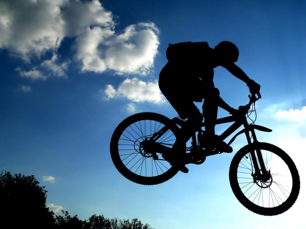 Silhouette of a cyclist performing a jump against a bright sky with clouds, showcasing dynamic movement and athleticism.