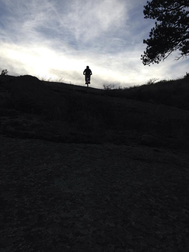 Cannondale RZ 120-1: A silhouette of a person standing on a rocky hillside against a backdrop of cloudy sky. The figure is positioned towards the top of the hill, surrounded by sparse vegetation.