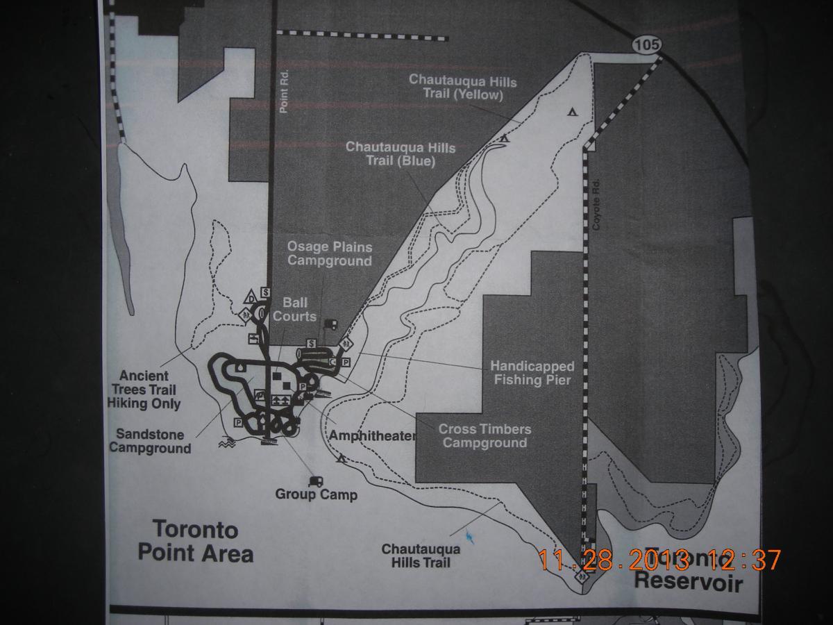 A black and white map of the Toronto Point Area, showing various hiking trails, campgrounds, an amphitheater, ball courts, and a fishing pier. Key features include the Osage Plains Campground, Ancient Trees Trail (hiking only), and several labeled trails in yellow and blue. A section labeled "Reservoir" is also visible, along with route markers and parking areas. Chautauqua Hills Trail mountain bike trail.