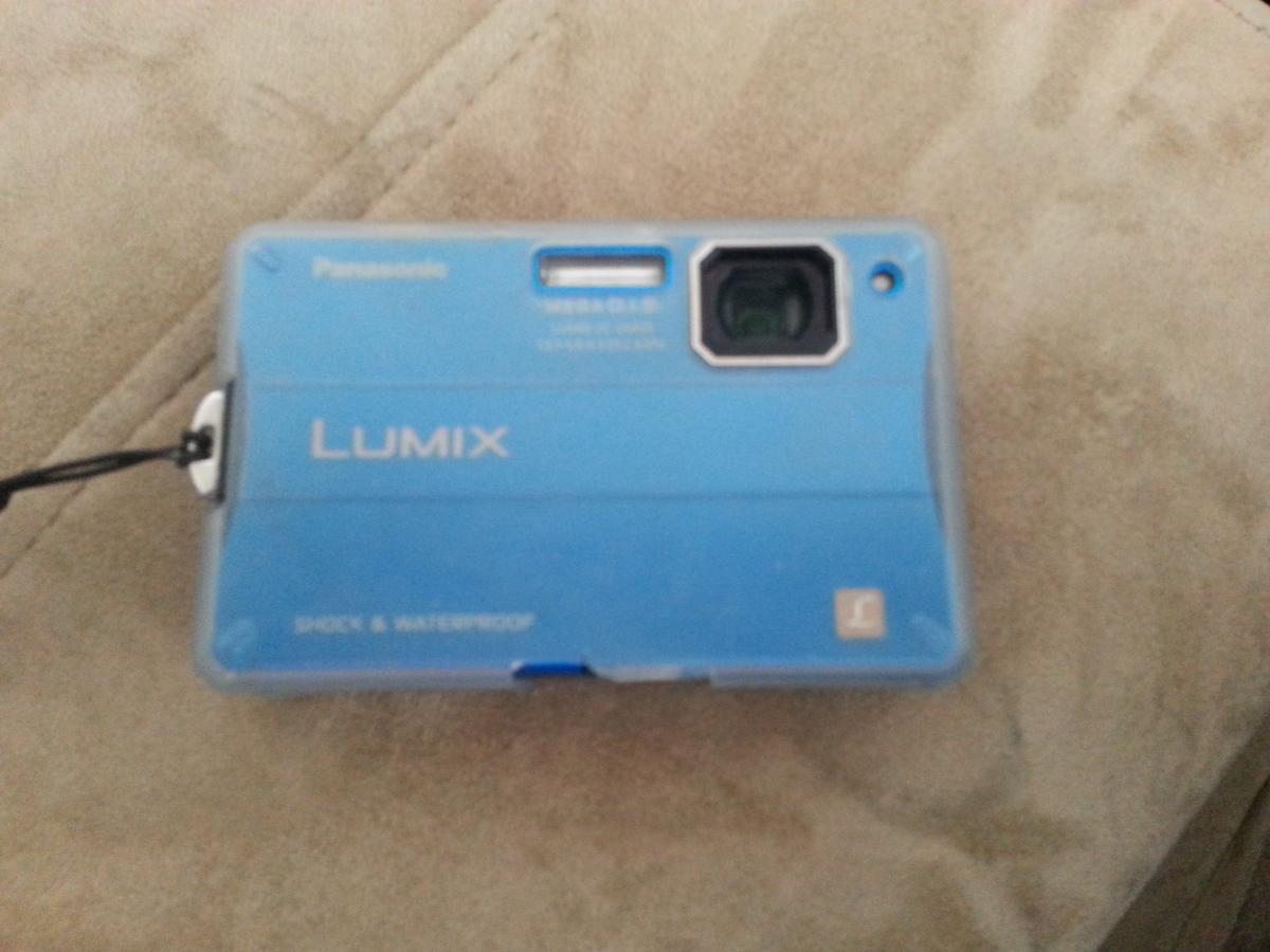 Panasonic Lumix DMC TS10: A blue Panasonic Lumix camera placed on a light-colored surface, showcasing its waterproof and shockproof design.