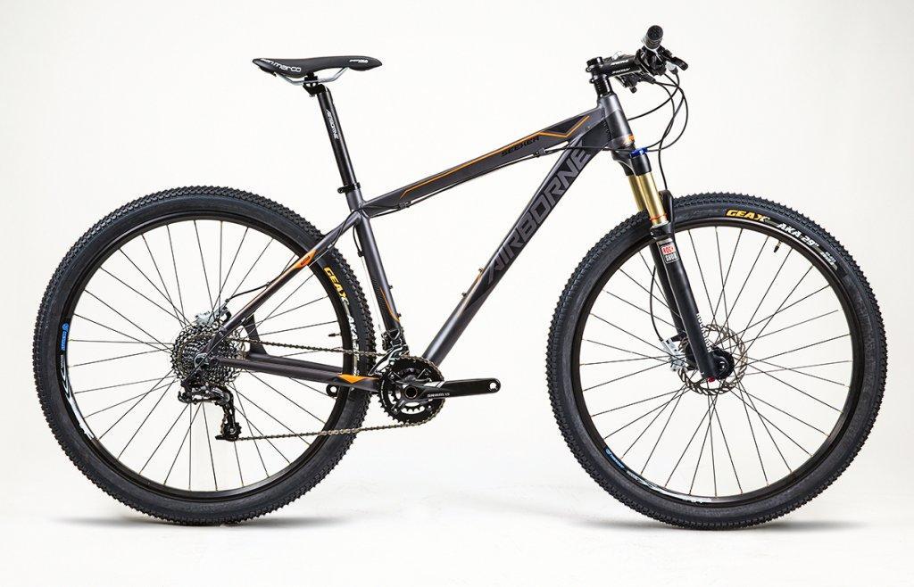 Airborne Seeker: A modern mountain bike with a sleek black and orange frame, featuring front suspension, disc brakes, and thick tires designed for off-road riding. The bike is positioned upright against a plain background, showcasing its sturdy build and high-performance components.