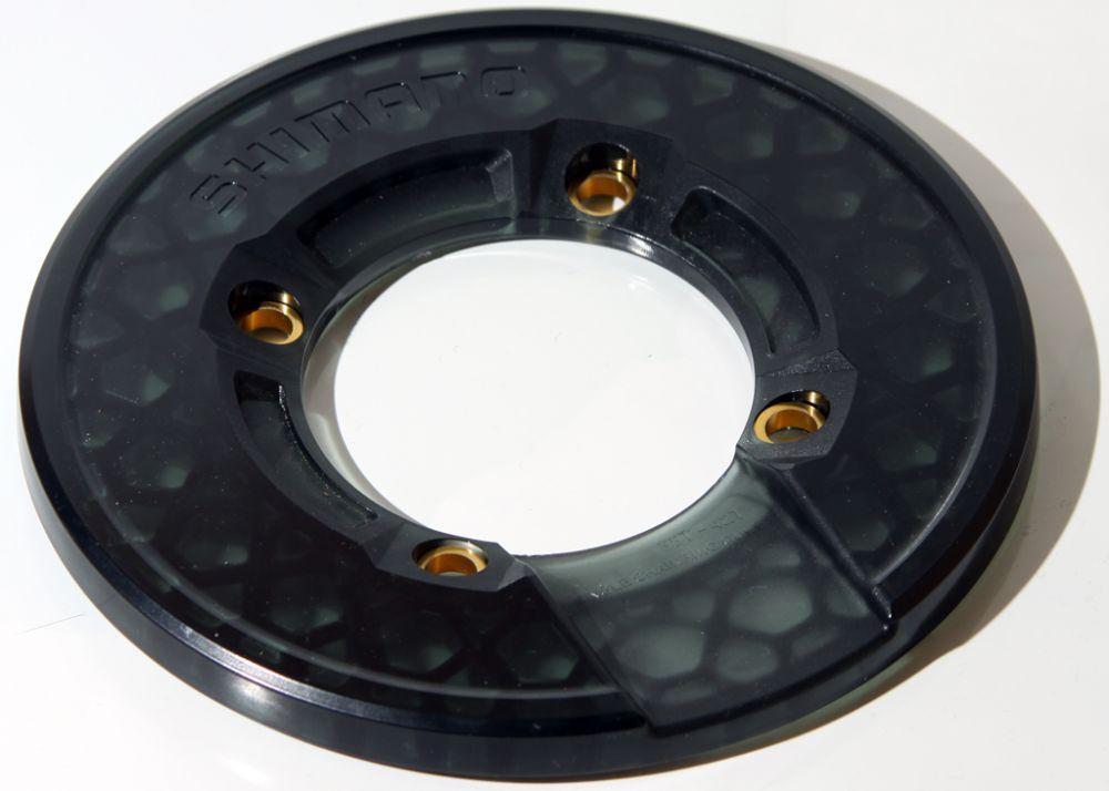 Shimano Saint Bashguard: Black bicycle component with a hexagonal pattern and gold accents, featuring a central hole and four attachment points, designed for mounting on a bike. The word "Shimano" is embossed on the surface.