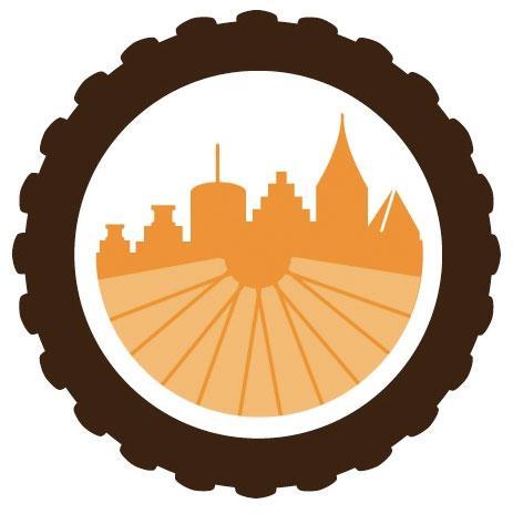 A stylized logo featuring a silhouette of a city skyline in orange, set against a circular emblem resembling a tire. The skyline includes various building shapes, and the backdrop features radial lines suggesting movement or a wheel.