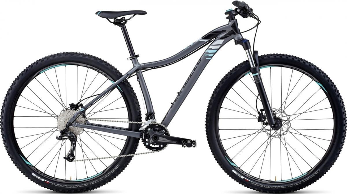 Specialized JETT 29: A modern mountain bike with a sleek gray frame, featuring thick tires suitable for off-road terrain, a front suspension fork, and a derailleur system for gear shifting. The bike has a minimalist design with turquoise accents on the frame and wheels.