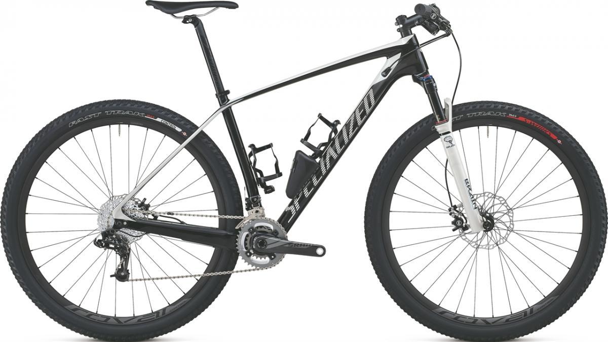 Specialized STUMPJUMPER MARATHON CARBON HT: A modern mountain bike featuring a black and white frame, front suspension, and wide tires labeled "Fast Trak." The bike is equipped with disc brakes, a gear system, and two water bottle holders, showcasing a sleek and sporty design.