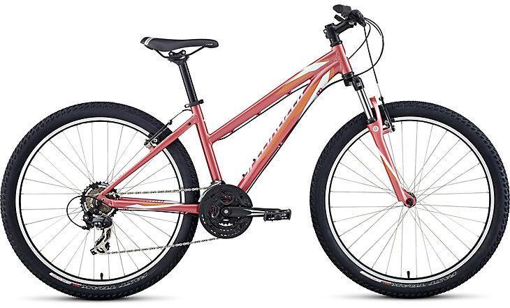 Specialized Myka 26: A pink and white mountain bike with a lightweight frame, featuring wide tires, a double chainring, and a front suspension fork. The bike is designed for off-road riding and has a sleek, modern look suitable for casual or adventurous riders.