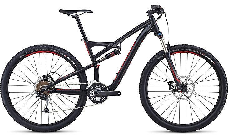 Specialized Camber 29: A black and red mountain bike with a dual suspension frame, featuring wide tires and disc brakes. The bike is positioned to showcase its side profile, highlighting the sleek design, gear mechanism, and suspension components.