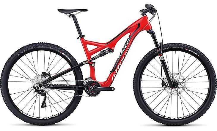 Specialized Stumpjumper FSR Comp Carbon 29: A modern mountain bike featuring a sleek red and black frame, equipped with wide tires, front suspension, and a gear system for off-road cycling. The bike is positioned against a plain background, highlighting its design and features.