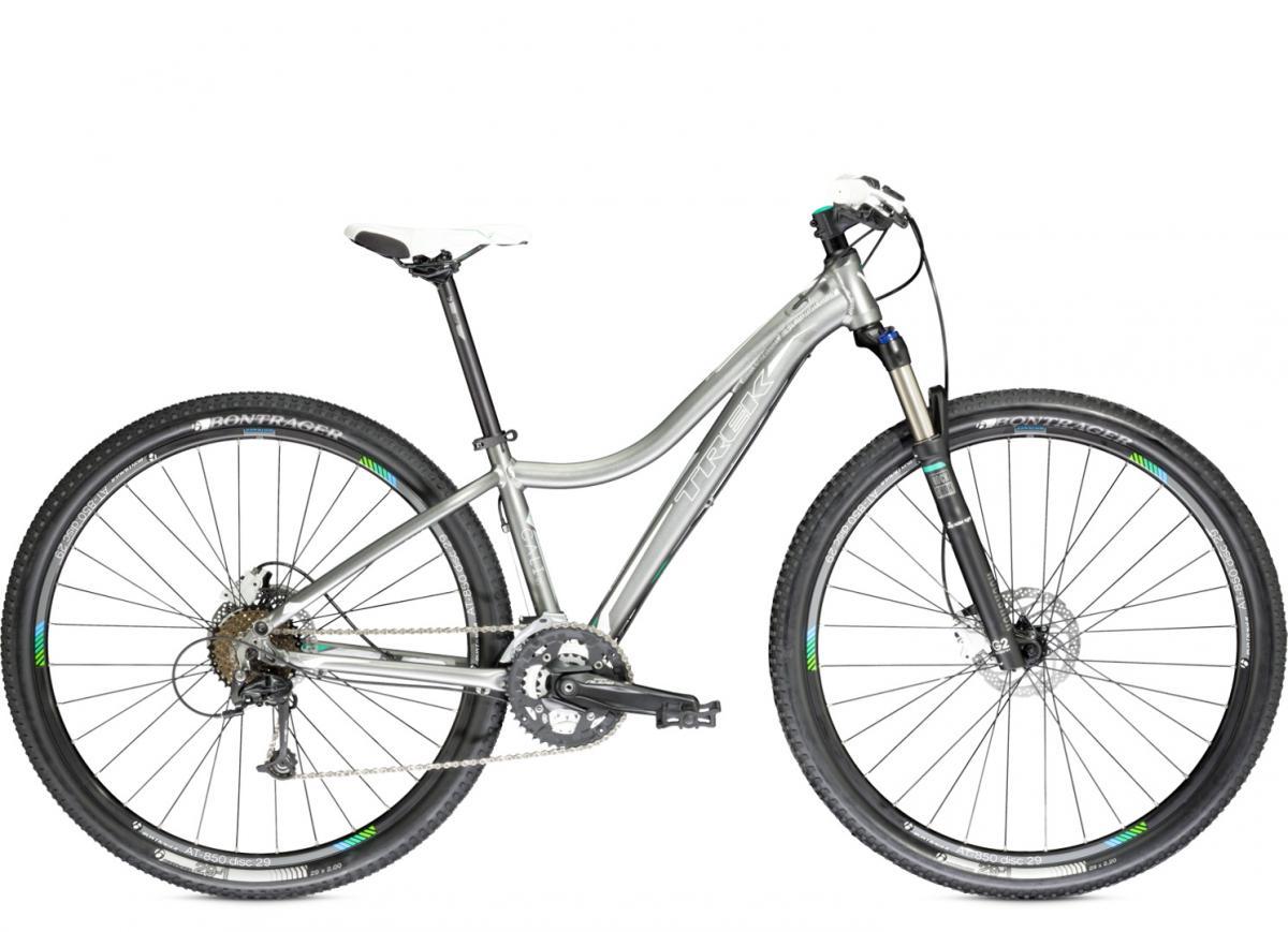 Trek Cali SL: A silver mountain bike with a sleek frame, front suspension fork, and knobby tires, positioned against a white background. The bike features a white seat and is equipped with a gear system visible on the chainstay.
