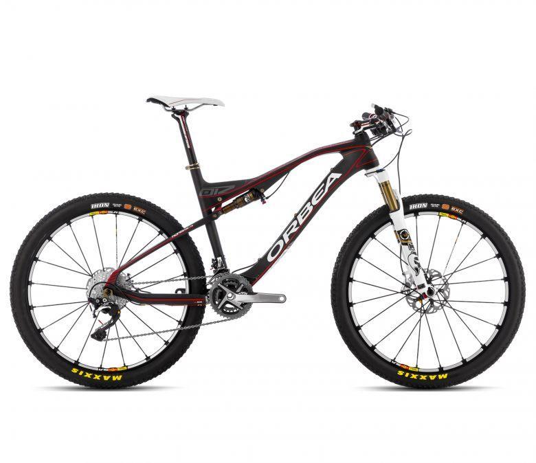 Orbea Oiz M-Team: A sleek black and red mountain bike with double suspension, featuring disc brakes and knobby tires. The bike has a lightweight frame and is positioned upright, showcasing its intricate components and design.