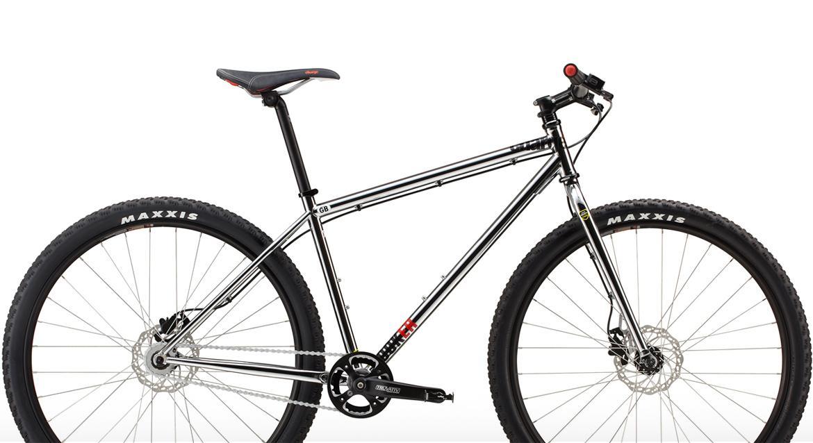 Charge Cooker SS: A sleek, silver mountain bike featuring a minimalist design, with a black seat and Maxxis tires. The bike has a sturdy frame, disc brakes, and a single gear setup, making it suitable for off-road riding. The overall appearance emphasizes durability and performance.
