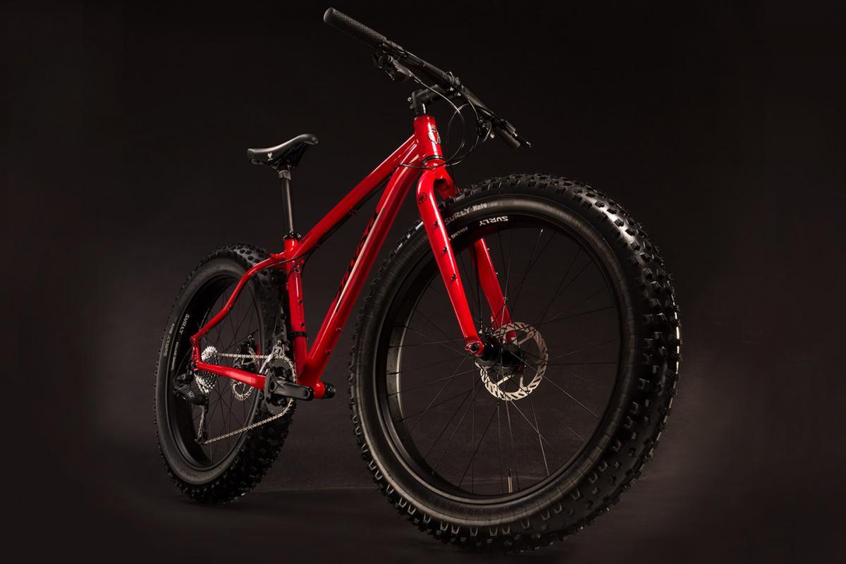Salsa Mukluk 3: A vibrant red mountain bike with wide tires, showcasing its sturdy frame and disc brakes, positioned against a dark background.