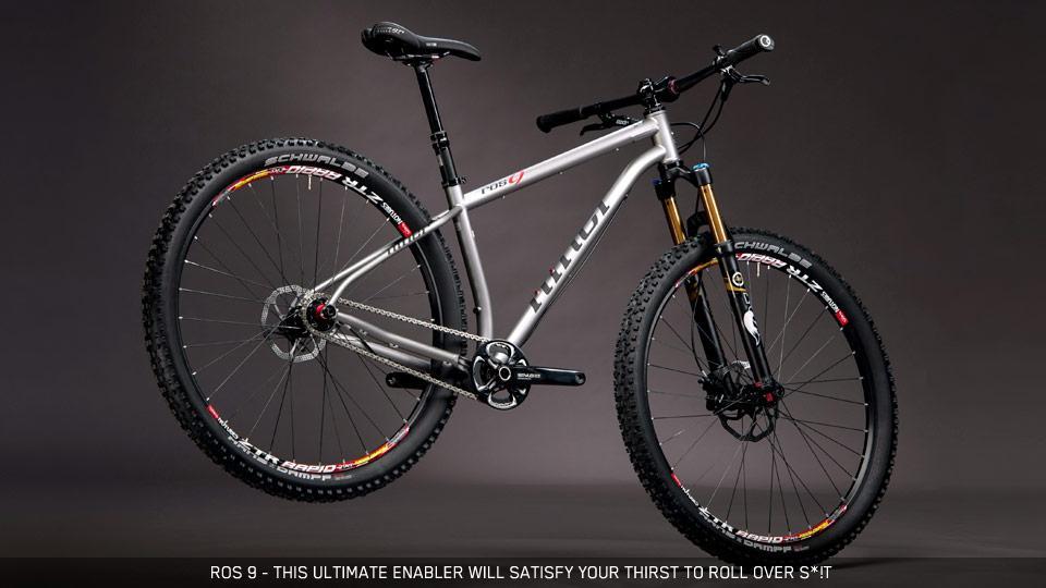 Niner ROS 9: A modern mountain bike featuring a lightweight silver frame, thick tires designed for off-road performance, and front suspension. The bike is presented against a dark background, showcasing its sleek design and quality components. The wheels have colorful branding on the sidewalls, highlighting their durability and traction for rugged terrains.