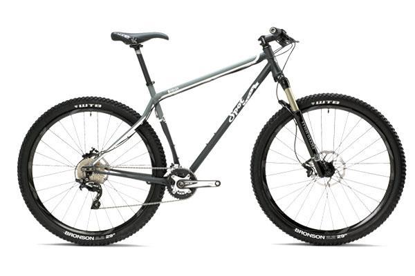 Spot Honey Badger Geared: A gray mountain bike with wide tires, a sleek frame, and a front suspension fork, positioned upright against a neutral background. The bike features dual disc brakes and a gear shifter on the handlebars.