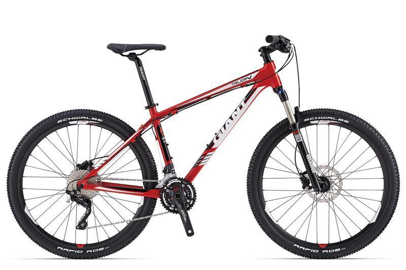 Giant Talon 27.5 1: Mountain bike in a vibrant red color with black accents, featuring wide tires, a sturdy frame, and a front suspension fork. The bike is designed for off-road cycling and includes components like a gear shifter and disc brakes.
