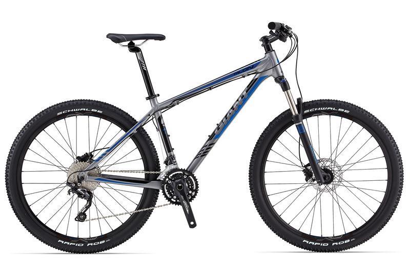 Giant Talon 27.5 2: A modern mountain bike featuring a silver and blue frame, geared for off-road cycling. It has thick, rugged tires labeled "Schwalbe Rapid Rob," a front suspension fork, and a 21-speed gear system, designed for stability and performance on various terrains.