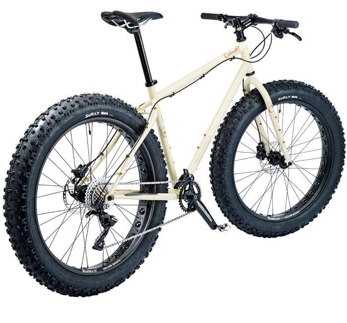 Genesis Caribou: Fat tire mountain bike with a cream-colored frame and oversized, textured black tires, featuring a single gear setup and a sporty design suitable for rugged terrain.