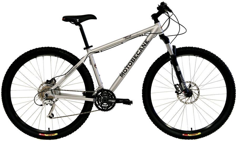 Motobecane Fantom 29PRO: A silver Motobecane mountain bike with aerodynamic frame design, large knobby tires, and front suspension. The bike features a gear system and disc brakes, positioned against a plain white background.