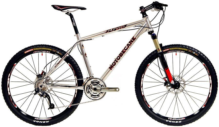 Motobecane FLY 9357: Alt text: A silver Motobecane mountain bike with prominent features including thick tires, disc brakes, and a sleek frame. The bike is positioned at an angle to display its components, including the gears and handlebars.