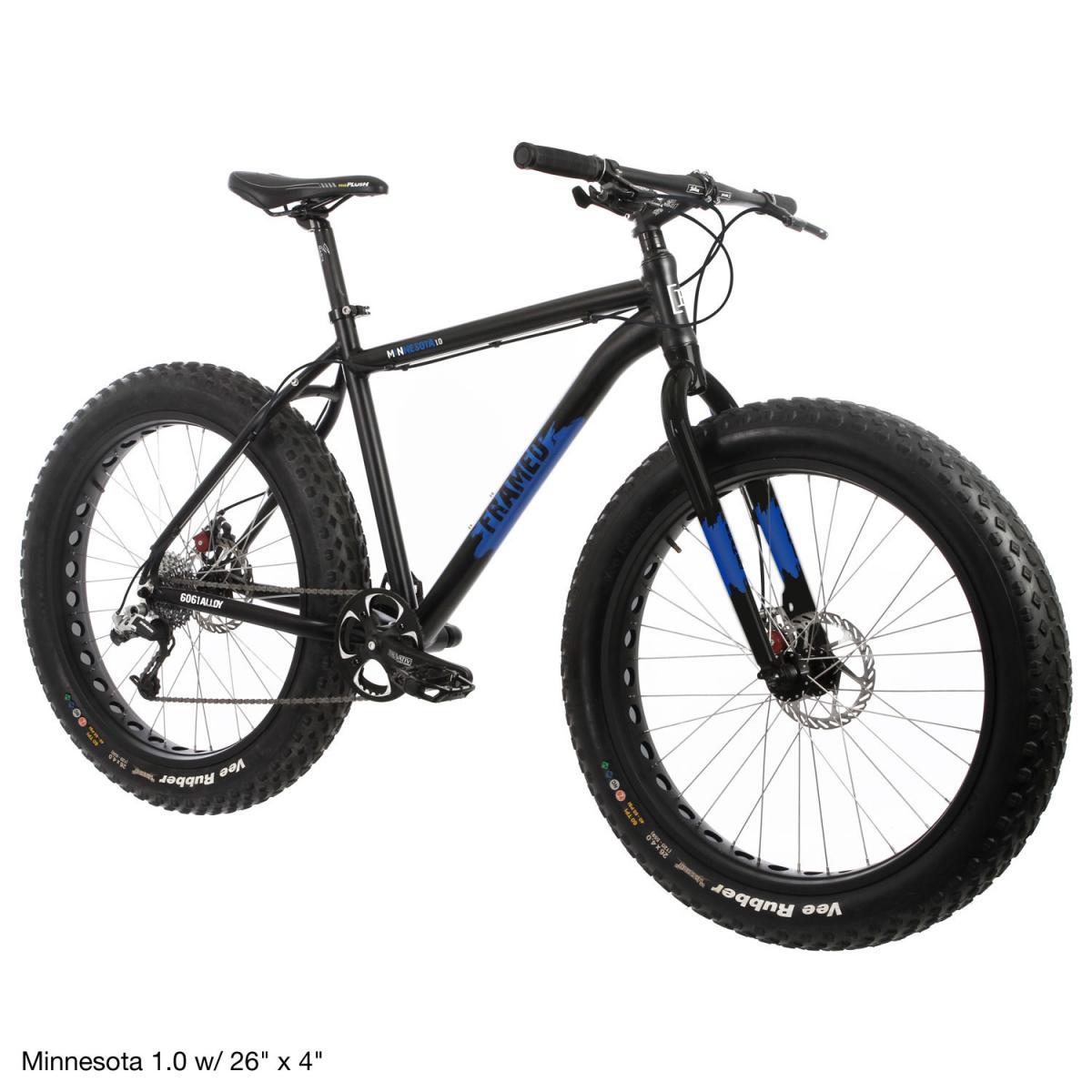 Framed Minnesota 1.0: A black fat bike with blue accents, featuring wide tires labeled "Vee Rubber," designed for off-road riding. The bike has a sturdy frame and components suitable for rugged terrain, showcasing its robust design.