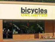 Exterior of a bicycle shop named "Bicycles Unlimited," featuring a display of bicycles in the window and a bright sign above the entrance.
