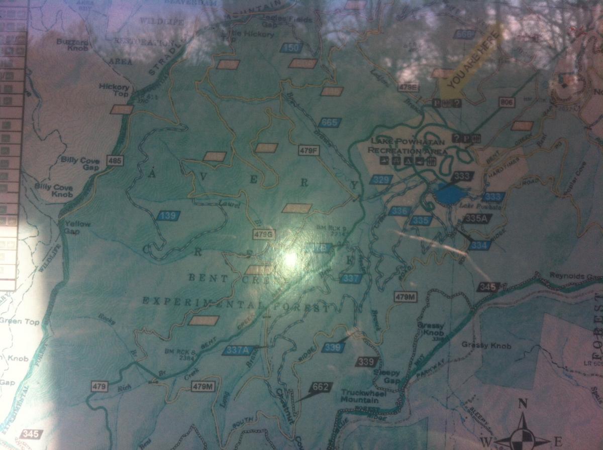 A detailed topographic map showing various trails, elevation lines, and features in a forested area, including locations such as Lake Powhatan Recreation Area, Bent Creek Experimental Forest, and nearby mountain peaks. The map outlines roads, paths, and geographic landmarks, with a "You Are Here" indicator. Bent Creek mountain bike trail.