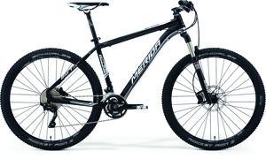 Merida Big.Seven XT-Edition: A black and white mountain bike with thick tires, a lightweight frame, and front suspension. The bike features disc brakes and a modern design suitable for off-road riding.
