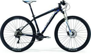 Merida Big.Nine 900: A black and blue mountain bike featuring a sturdy frame, disc brakes, and wide tires, positioned against a white background.