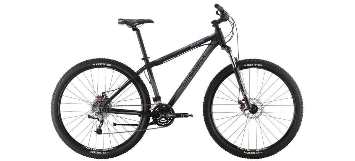A black mountain bike with wide tires, featuring disc brakes and a sleek frame design. The bike is displayed from the side, showcasing its geometry and components, including a suspension fork and multiple gears.