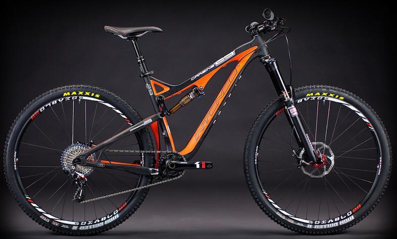 Intense Carbine 29: A modern mountain bike featuring a sleek design with a black and orange frame. It has high-quality components, including front suspension forks and disc brakes. The bike is mounted on thick tires suitable for off-road terrain, against a dark background.