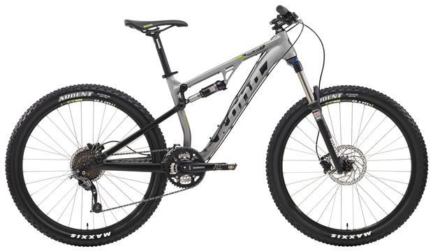 Kona Precept DL: A modern mountain bike with a silver and black frame, featuring thick tires and a front suspension fork. The bike has disc brakes, a wide handlebar, and a sleek design suitable for off-road riding. The wheels are equipped with Maxxis tires, indicating durability for various terrains.